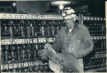 'Coal miner Harmon Neal, an electrician at the Cannelton No. 8 mine in Fayette County, West Virginia, takes off his coat at the mine's lamp house Thursday night. Neal was leaving work to join fellow members of the United Mine Workers union, which began a nationwide strike at 12:01 a.m. Friday. (AP Laserphoto) (hwr6040mbrCNDM/Craig Cunningham) (1981) (See AP wire story PM-UMW Strike, Bjt.)'