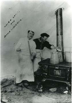 Two men cook on a stove in a tent.