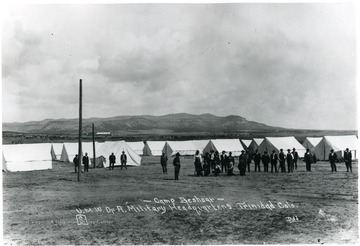 Group of men stand in front of tents.