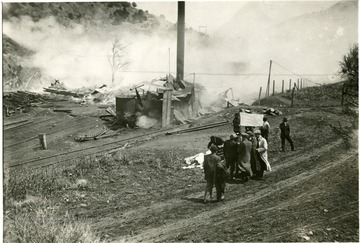 Men surround a white flag while the remains of building smolder in the background.