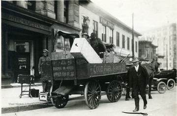 Colo. Fuel and Iron Co. horse drawn cart with a coffin in the back. The cart is parked in front of the Majestic and Fisk Tires buildings.