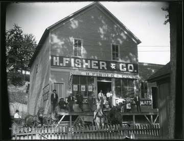 Men, women, and children standing in front of the H. Fisher and Co. Store.  Horse drawn carriages are also in front.