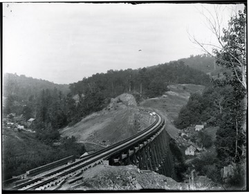 A railroad bridge crosses a valley with a couple of buildings to either side.