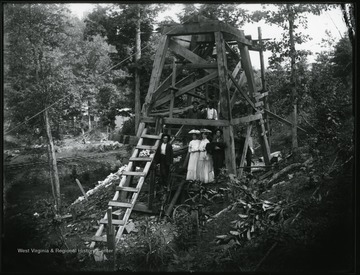 Five men and two women standing under a wooden derrick.