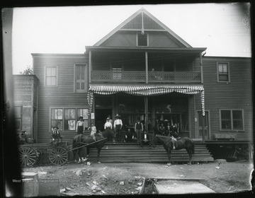 Group of people standing in front of a building.  Horses also in front of the store.