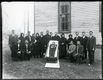 Mourners standing near the open casket of a man next to a church.