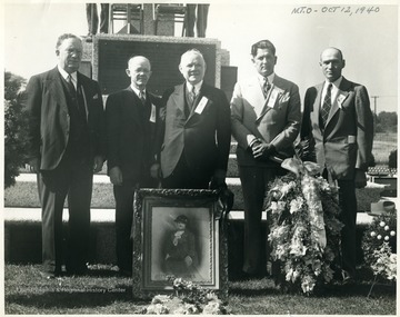 Group portrait of five men with standing in front of the Mother Jones Memorial.  A framed portrait of Mother Jones sits on the ground in front of the group.