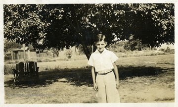 Boy standing by himself, tree in the background. Photograph from Joe Ozanic scrapbook.