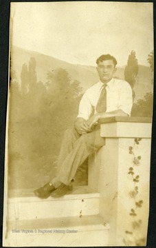 Portrait of an unidentified man wearing a shirt and tie sitting at the top of a stairway.  