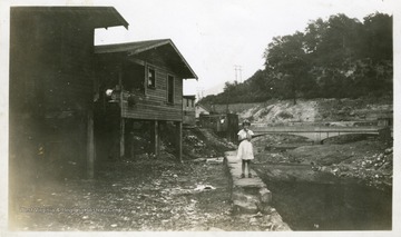 Small girl standing on a rock wall beside buildings and a small creek.  