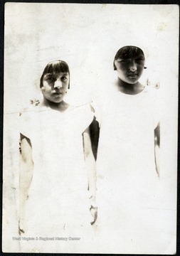 Two young girls standing together, wearing bonnet like hats. 
