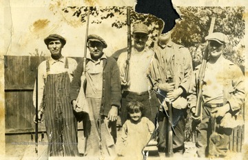 Five men holding guns and boy standing in front of them. 