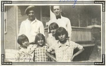 Two men and four girls standing in front of a porch. 
