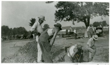 Men stand around the opening while men with shovels excavate the grave of Mother Jones.