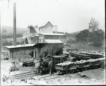 View of Limestone Plant with train engine and cars loaded with rocks.  Crew members stand throughout.