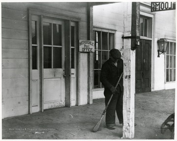 Mr. Hardin using a broom to sweep in front of the Arthurdale Post Office.  'Mr. Hardin, a former miner now handy man at Reedsville.  He has done all the landscaping and takes great pride in the appearance of his project.'