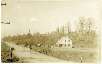 One house sits by the road while another overlooks it from the top of a hill.