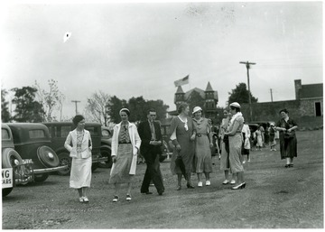 Visitors stand in a parking lot near parked cars at Arthurdale.  The Arthur mansion is visible in the background.