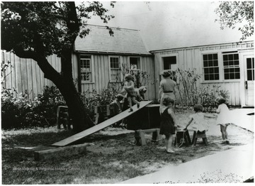 Children playing in the grass and with wooden benches.  One child walking down a wooden plank.