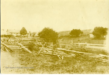 View of a house and buildings.  Wooden fence and trees in in foreground.