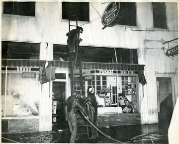 Three firemen putting out a fire at Rexall Drug Store.