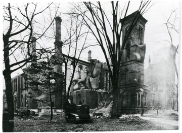 Trees in front of the ruins of the Capitol Building after the 1921 fire.  Men seated on a vehicle in front of the building.