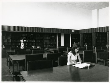 Girl sitting at a table in the Reading Room.  Another girl looking at a book from a shelf.  'The Library Reading Room is one of the many offerings of the West Virginia Library Commission in the Science and Culture Center.  The Commission maintains over a quarter-million sources for public use.  With its move to the Center, this is the first time that all elements of the State Library Commission have been housed under one roof.'