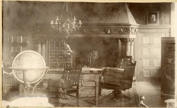 Interior of an elaborate living room with chairs, a fire place, a chandelier, and a globe of the world.