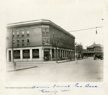 A few people are walking outside the Davis Trust Comapny. The Western Maryland Depot is visible beyond the Trust Company on Third Street in Elkins, West Virginia.