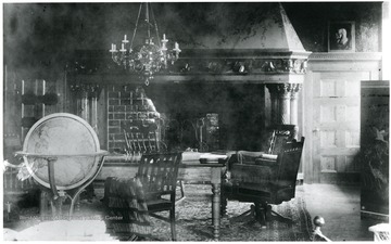Interior of the elaborate living room in Halliehurst with chairs, a fire place, a chandelier, and a globe of the world. 