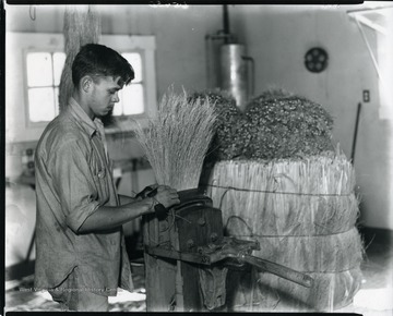 A man with a broom in a press at the Reliable Broom Plant in Grafton, West Virginia.