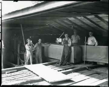 Workers at the Woodyard Lumber Company on West Main Street in Grafton, West Virginia. The photograph was taken in the shed as a log is being cut into  boards. L to R: Ralph Woodyard (son of owner), Edwin Woodyard (son of owner), unidentified worker, Bill Woodyard (son of owner), and W. A. Woodyard, owner. The lumber company was owned and operated by the Woodyard family until 1990. The property was sold and the building was razed in 1992.
