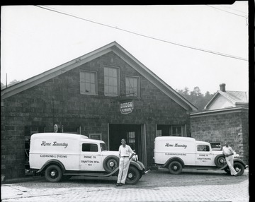 Two employees are standing in front of Home Laundry trucks next to a Dodge / Plymouth Garage in Grafton, West Virginia.