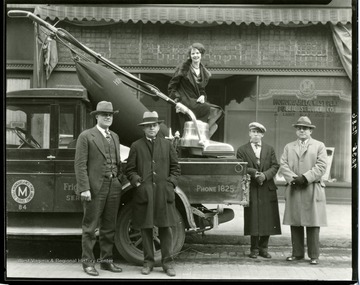 Four men stand below a girl seated on a large Hoover vacuum cleaner on the back of a Monongahela West Penn Public Service Company truck.
