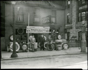 Three men standing outside in front of a Seiberling All Treads tire display at the Wolfe Tire Shop on Main Street in Grafton, W. Va. 