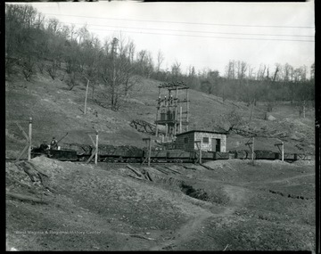 Two miners ride the locomotive leading a train of filled coal cars.