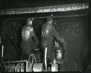 Two miners are working with a machine in an unidentified coal mine near Grafton, West Virginia.