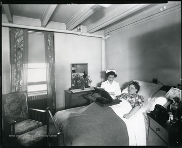 Woman lying in a hospital bed being attended by a nurse in Grafton, W. Va.