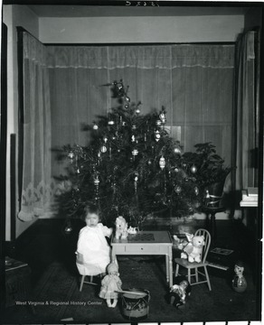 Girl sits at desk with dolls and other toys.