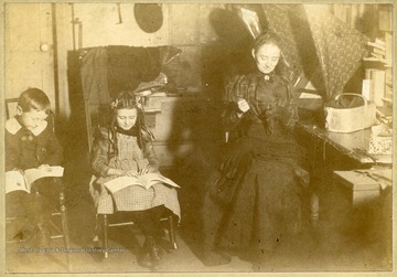 L.J. Loar Sr. and Grace Loar reading books, while Mrs. W.R. Loar is sewing.