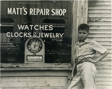 A young boy leans against the outside of a fix-it shop in Ohio County.