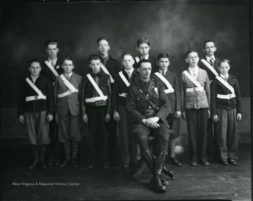 Young boys dressed in uniform stand behind a man dressed in uniform.