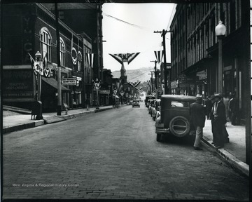 A view of Grafton, West Virginia from the corner of Lafayette Street and Main Street. Three gentlemen are talking while other people are window shopping.