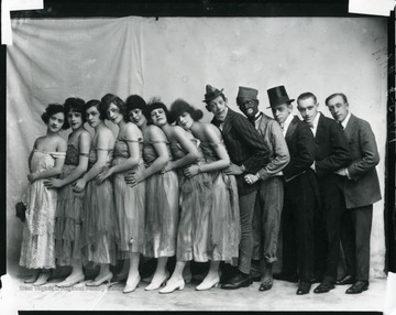 Seven female entertainers, two clowns, a man wearing a top hat, and two other male entertainers are standing in a line.