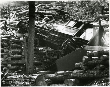 Three men stand amongst the wreckage of a train and piles of logs.