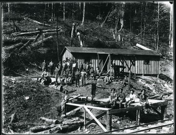 The crew stands and sits next to a wooden building.