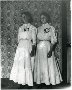 Two women standing together in front of wallpapered background.  Helvetia, W. Va.