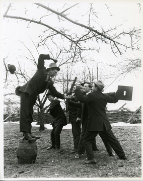 Group of men with arms raised ready to fight.  One man stands atop a barrel.