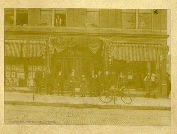 'Going from left to right, they are: Ersine Garland, visitor; Robert Wood,clerk; Roscoe McClure, clerk; T.S. Scanlon, Prop.; Bertha Mc Carthy, Boss; P.G. Dudley, B.K.; Jos. McCarthy, Mngr.; H.E. Gillilan,traveling-man; Mr. Brinker,visitor; and Hon. Peter Wippel, the fat shoe maker.' 