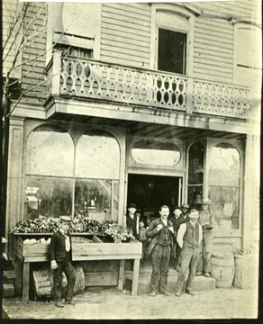 Men stand outside storefront. 'West side of 10th St. between 6th and 7th Avenues.'